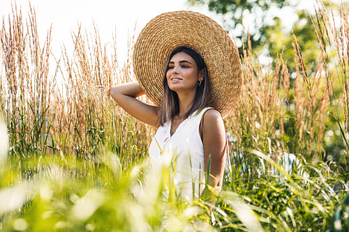 Young blond woman holds her straw hat while walking on the field