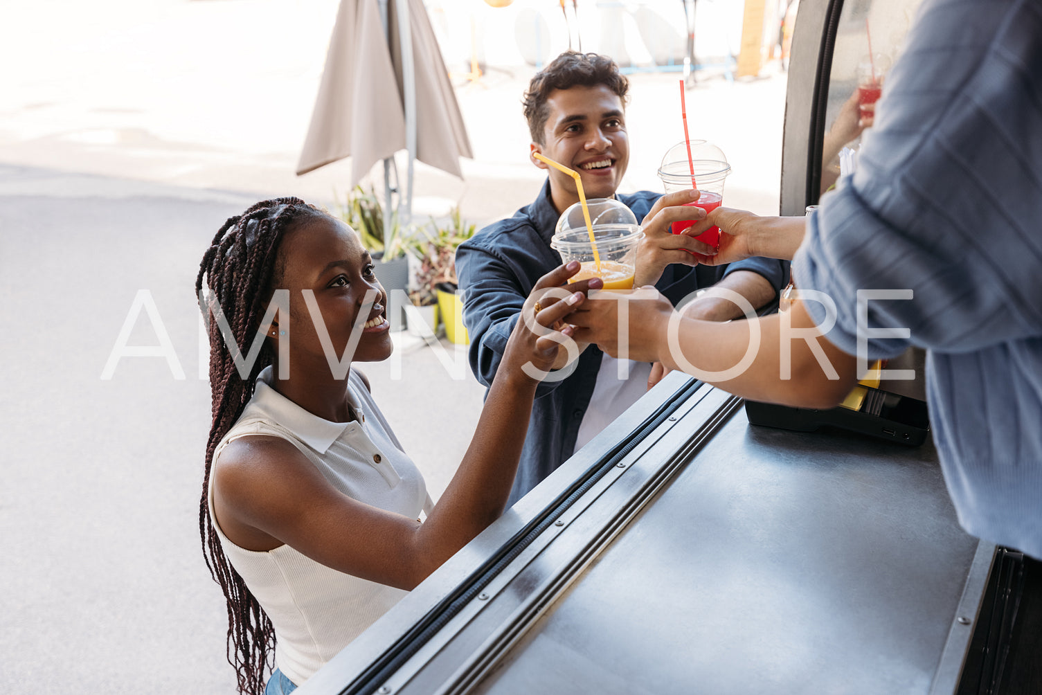 Two smiling customers receiving juice from unrecognizable saleswoman at a food truck