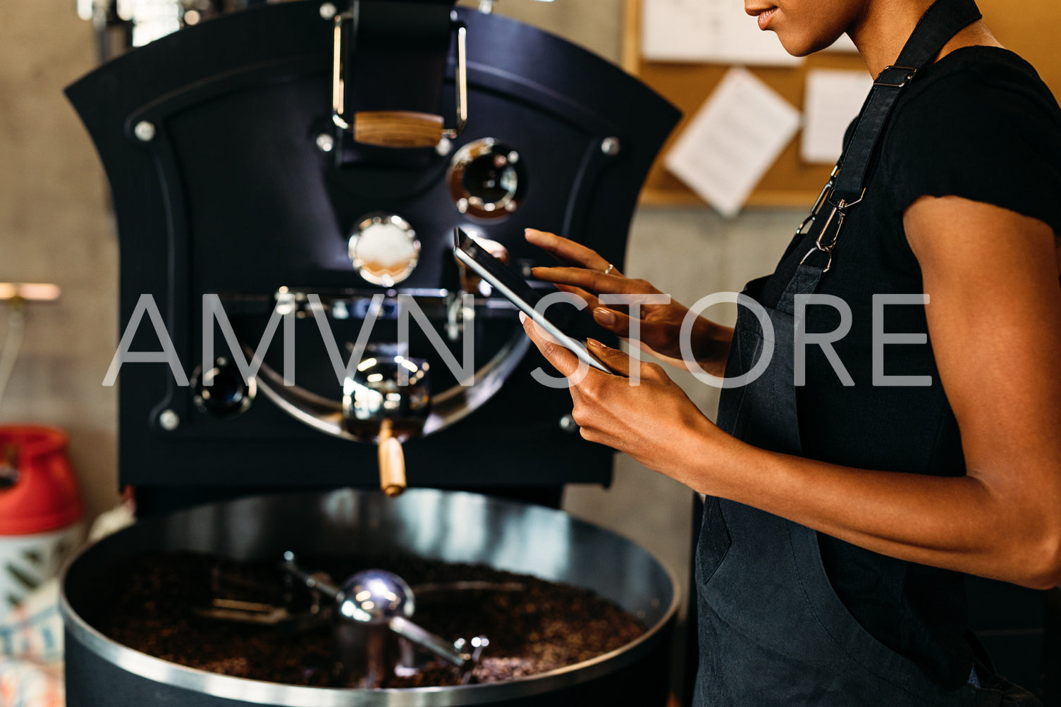 Female barista using digital tablet, standing near coffee roasting machine	