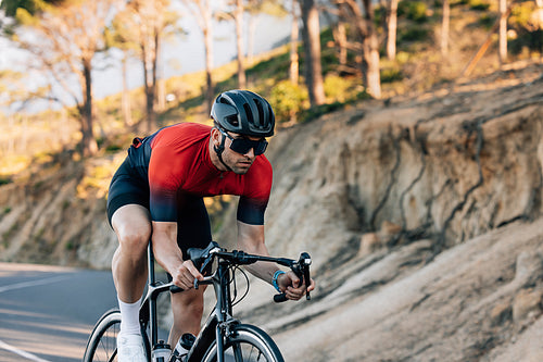 Professional cyclist going down a hill. Athlete in helmet and glasses riding road bike outdoors.