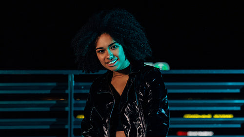 Smiling girl standing outdoors under neon lights and looking at camera