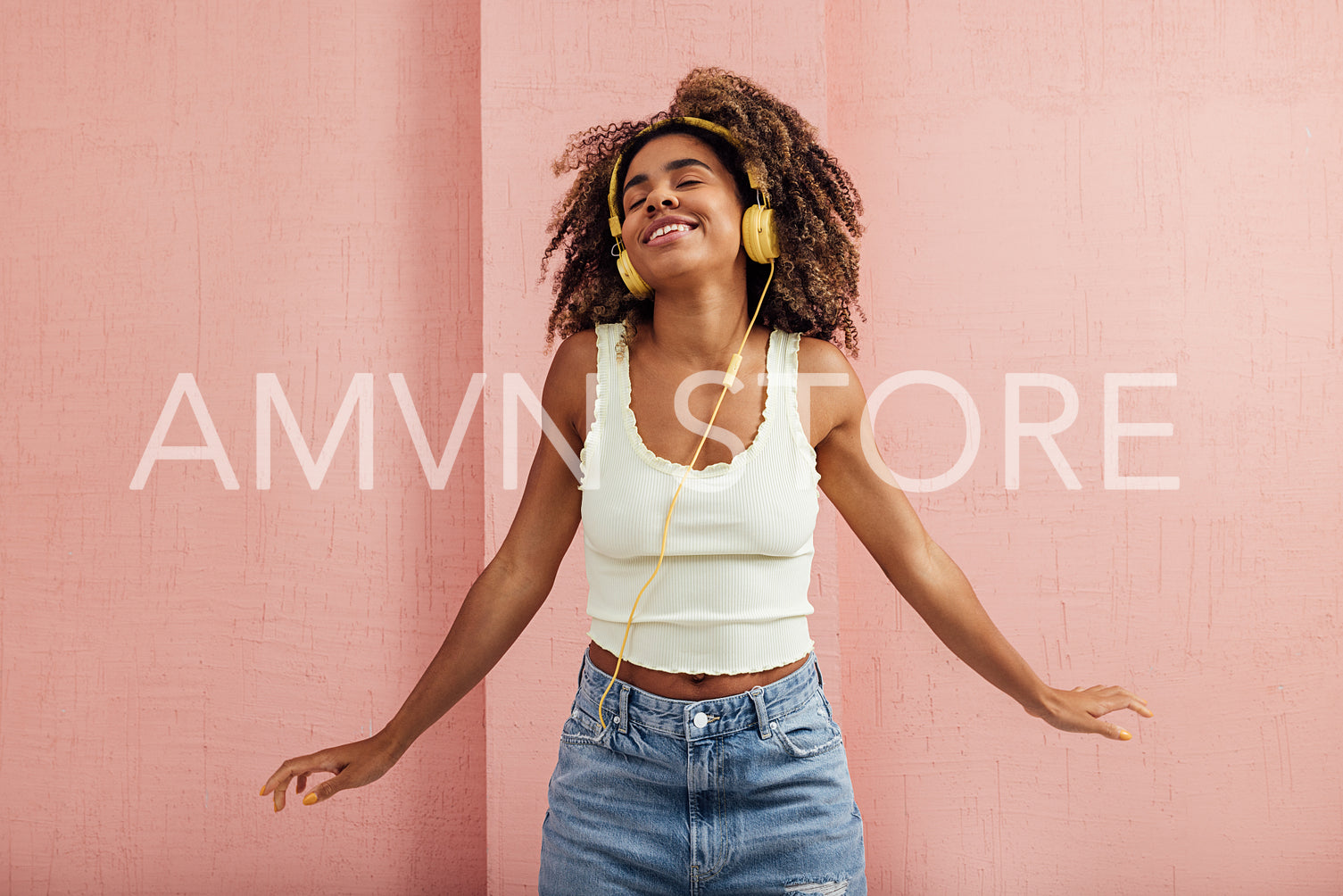 Happy woman enjoying music while standing at pink wall with clos