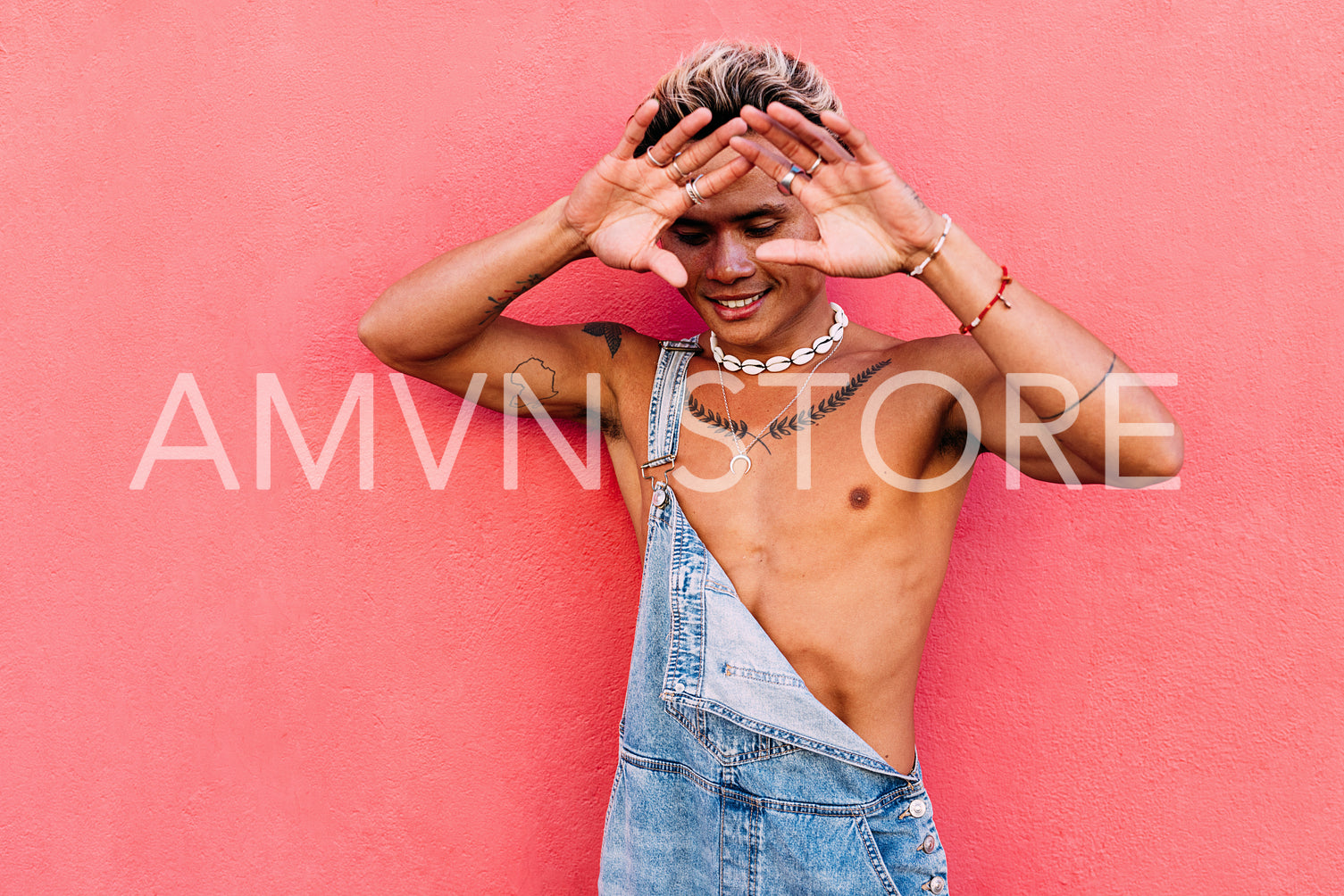 Handsome guy in casuals with bare chest hiding his face with palms at pink wall outdoors