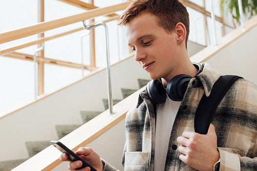 University student looking at his smartphone while standing at staircase