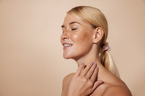 Side view of smiling woman with freckles standing with closed ey