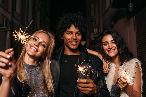 Group of friends standing on sidewalk at night, holding sparklers