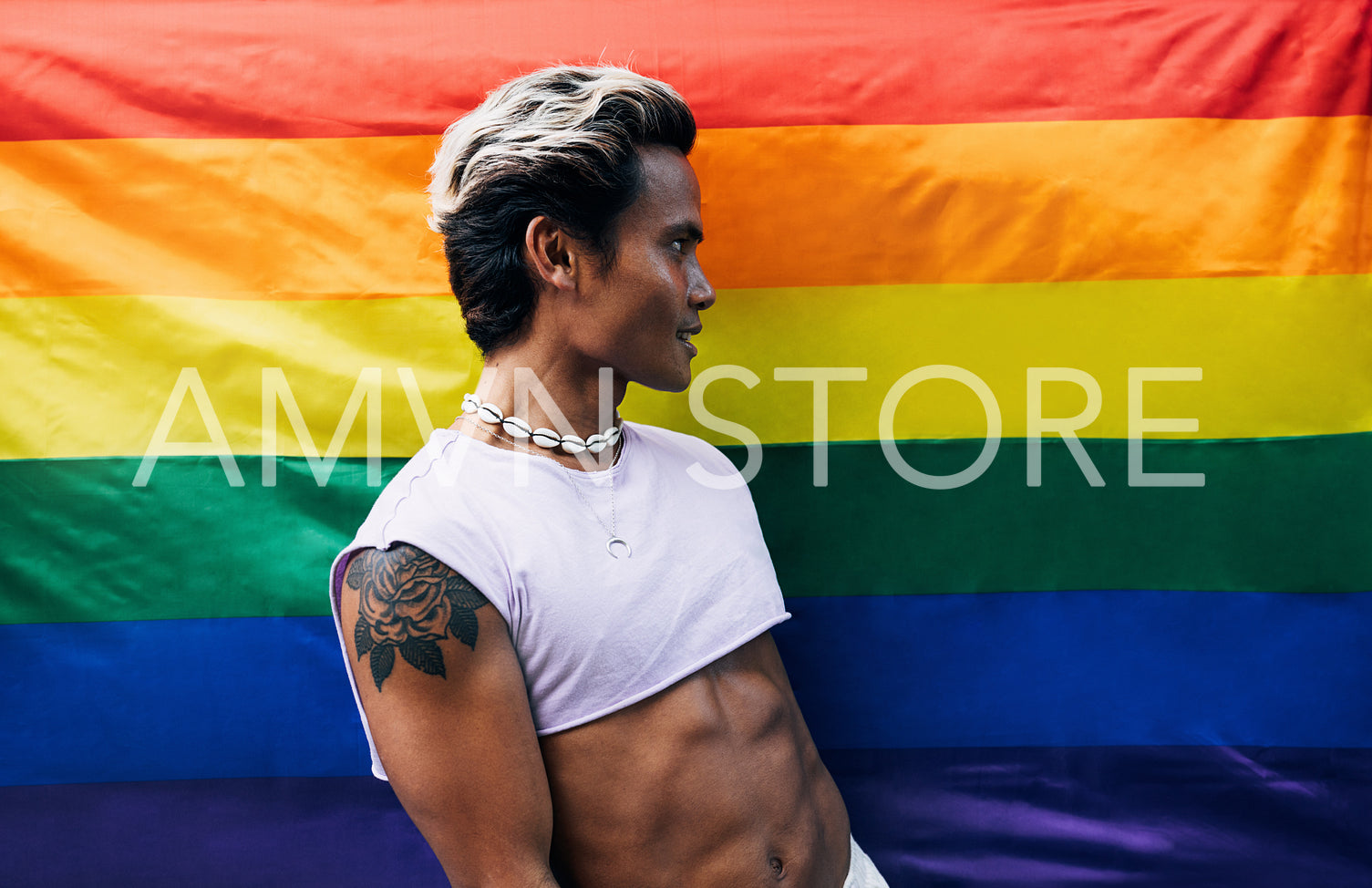 Side view of young stylish guy standing against LGBT flag and looking away