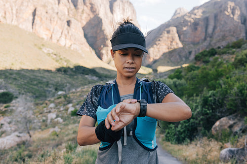 Young woman hiker checking smart watch while standing in valley