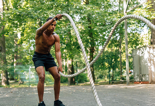 Side view of young man exercising with battling ropes outdoors