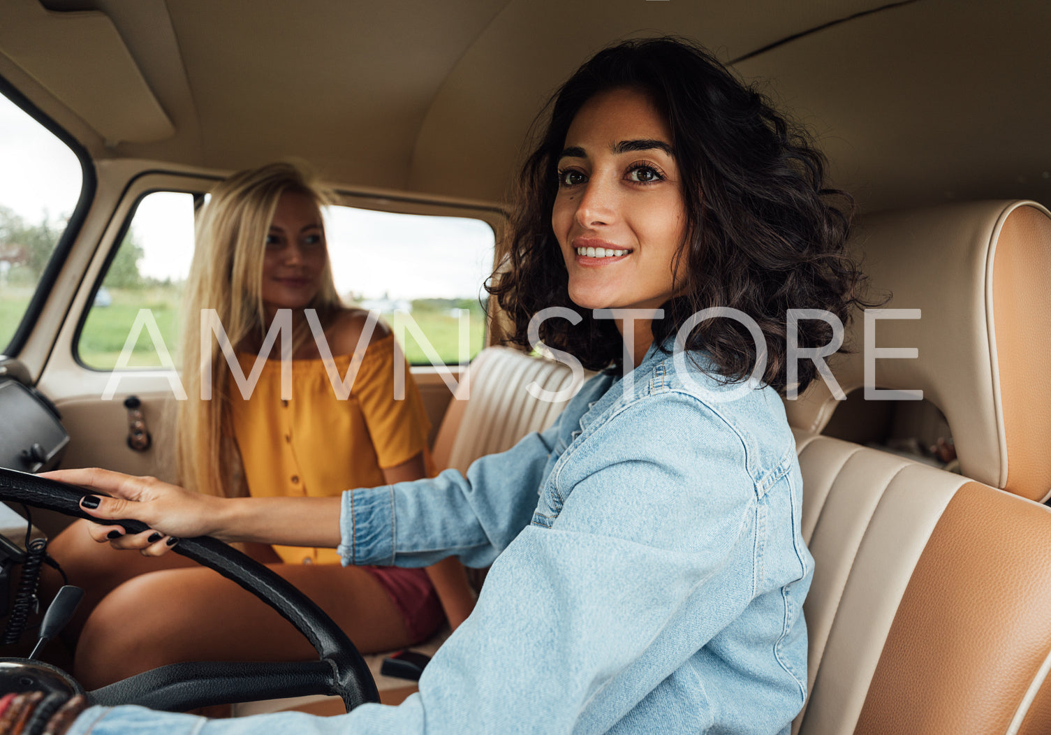 Smiling woman looking outside the car window while driving a van. Women friends enjoying on a road trip.