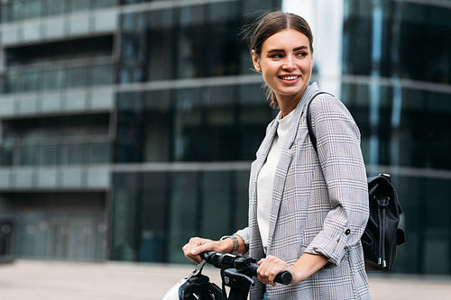 Happy woman in formal wear holding the handlebar and looking away while standing against an office building