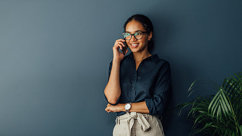 Smiling entrepreneur leaning to a wall in living room while talking on cell phone