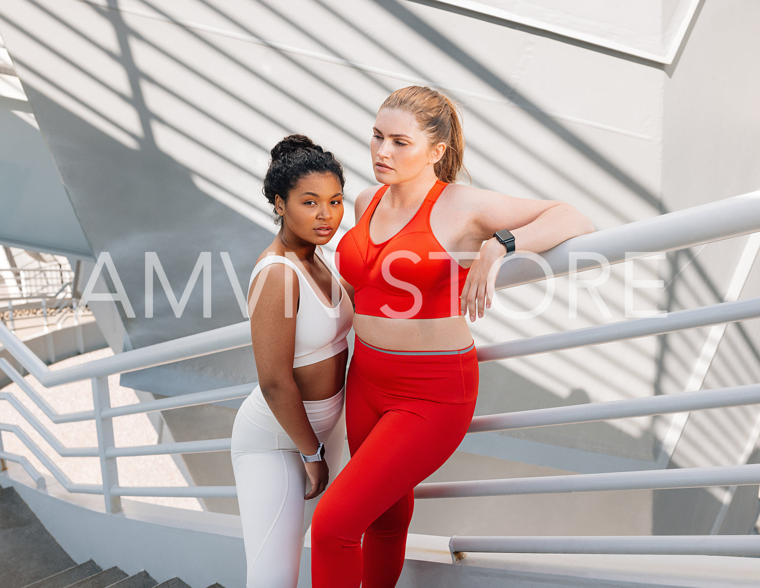 Two plus-size women standing at the railing relaxing after an intense workout outdoors. Young females in sportswear with plus-size bodies standing together.