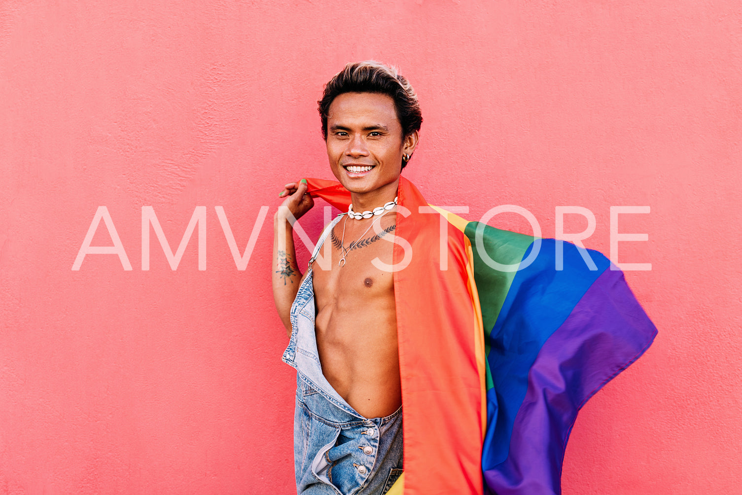 Happy male wearing overalls holding LGBT flag and looking at camera