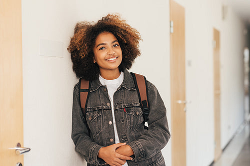 Young student with backpack smiling in high school leaning a wall