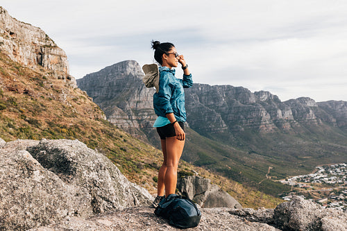 Young woman hiker holding sunglasses and relaxing while looking at view during hiking