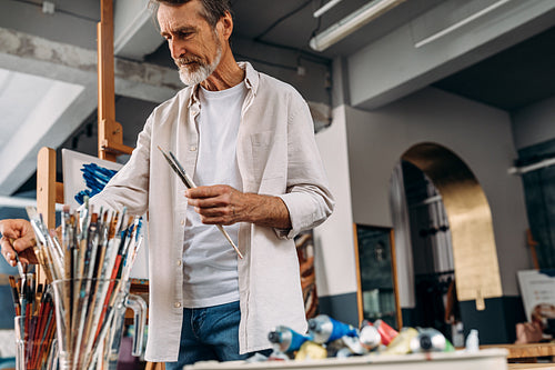 Senior artist standing in studio picking paintbrush for drawing