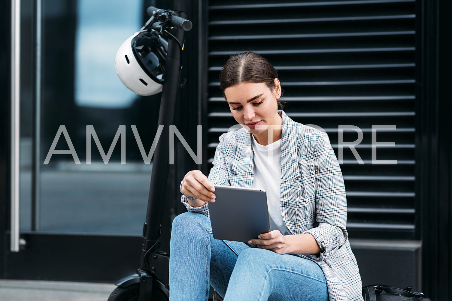 Beautiful caucasian female sitting on parked electric scooter on street holding a digital tablet