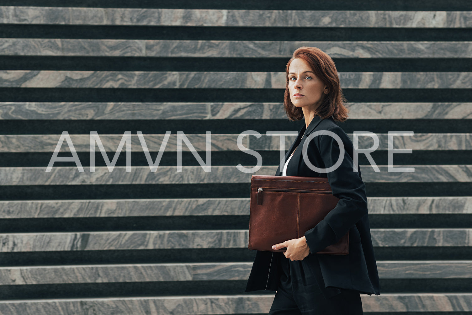 Side view of a confident businesswoman with a leather folder walking outdoors. Middle-aged businesswoman in black formal clothes looking away while walking.