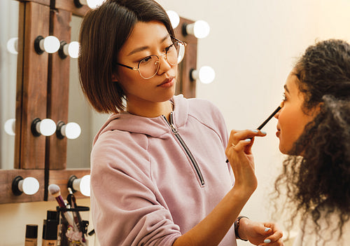 Young woman applying cosmetics with brush on model eye