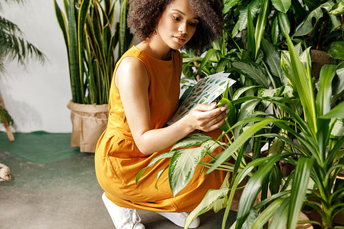 Young woman holding a book and observe a plant in workshop