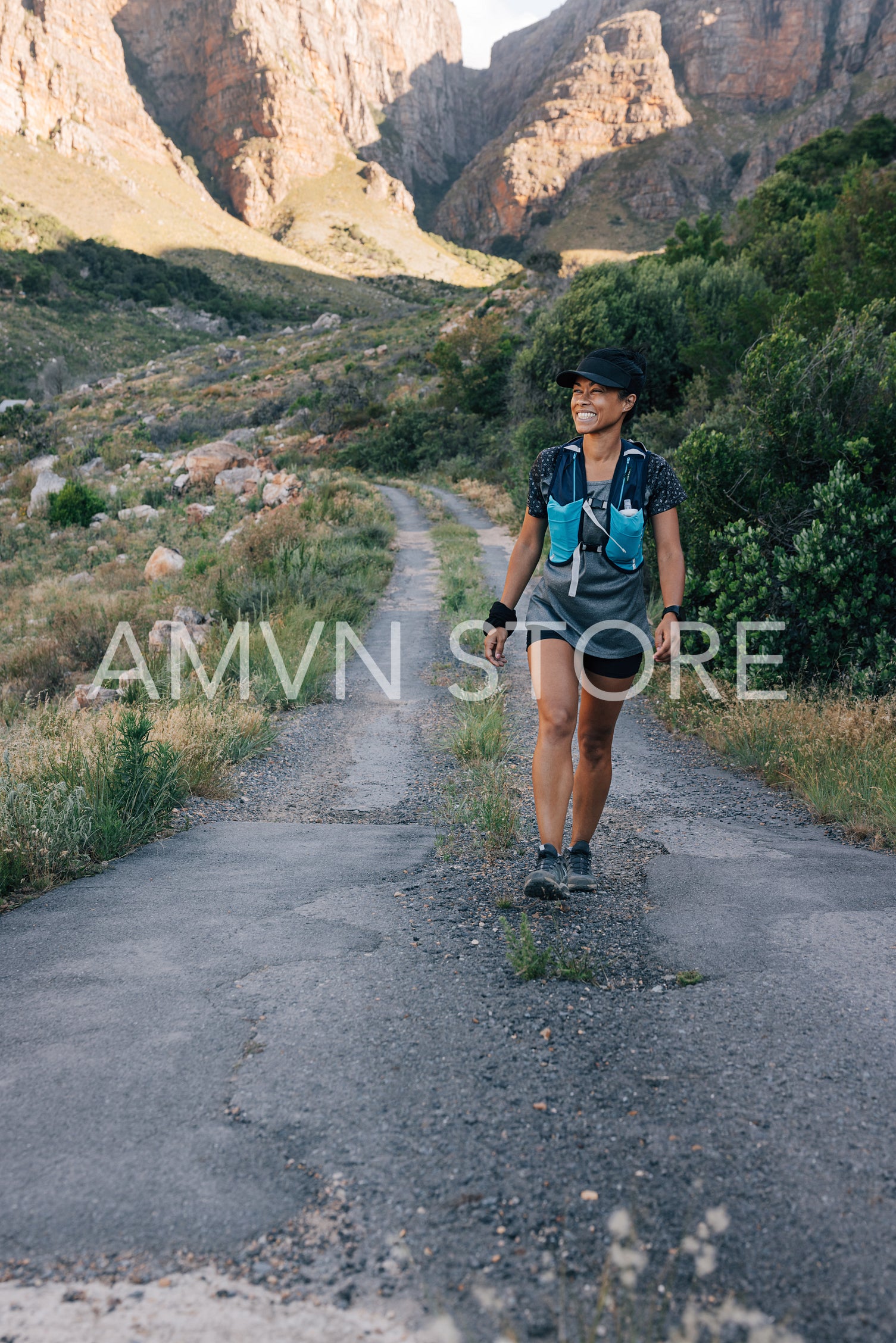 Smiling woman on hike. Female in sportswear walking on a road in valley and looking away.