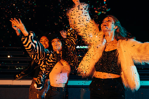 Happy girls throwing confetti at night