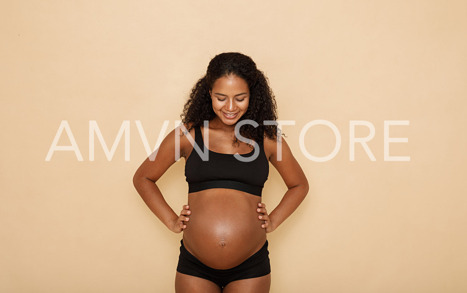 Smiling pregnant woman standing in studio and looking at her belly	