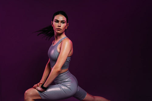 Young woman in silver sportswear flexing her body before exercises against magenta background