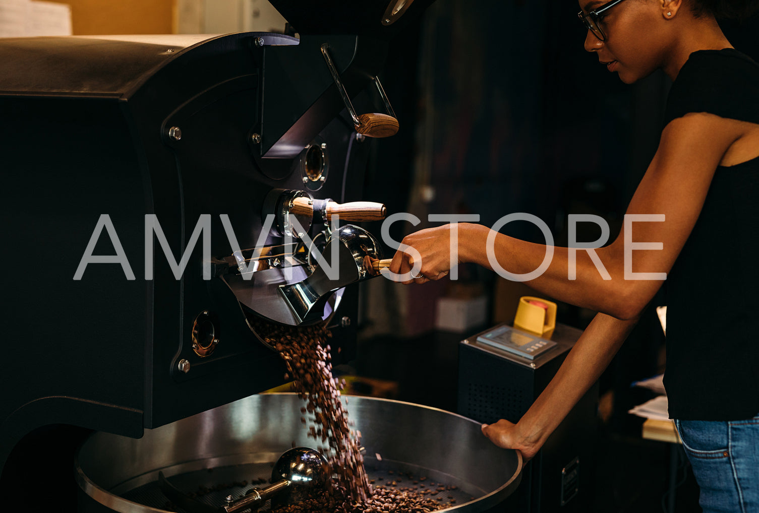 Young barista opening a coffee roaster, beans falling out into the cooling pan