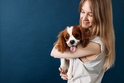 Young smiling pet owner holding her cute little dog in studio ag