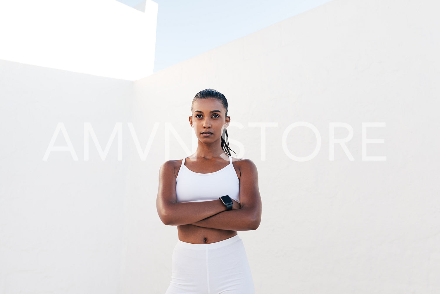 Young confident female athlete looking into a distance outdoors. Fit woman with crossed arms relaxing during a workout.