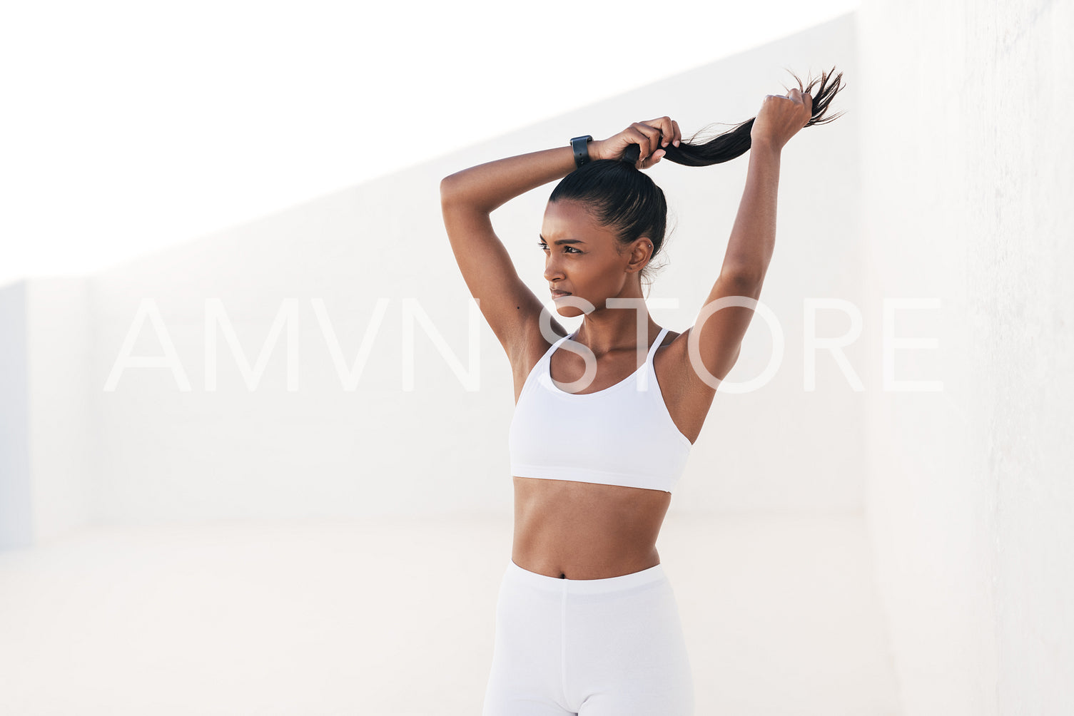 Slim woman athlete adjusting her ponytail while standing in outdoors studio