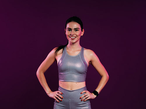 Confident woman in silver fitness attire at magenta backdrop