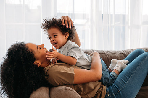 Mother playing with cute son at home. Side view of laughing boy