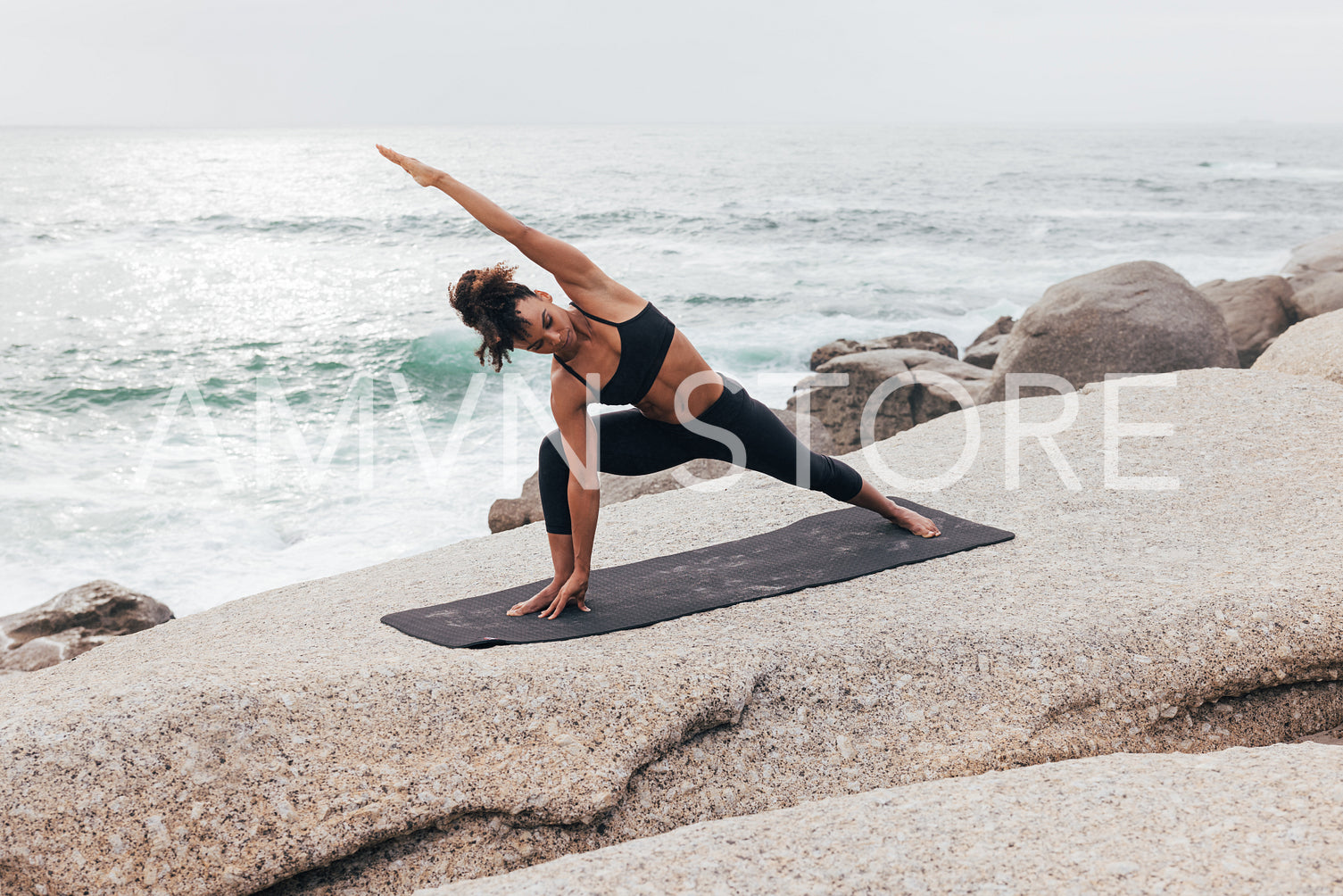 Woman practicing Extended Side Angle Pose by ocean at sunset