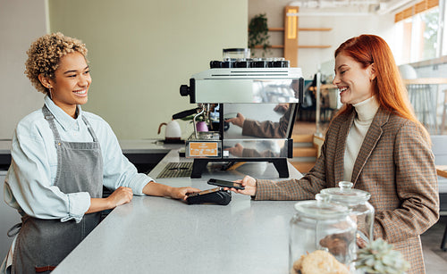 Happy client paying by mobile phone in a coffee shop. Side view of a business owner and a client making a transaction.