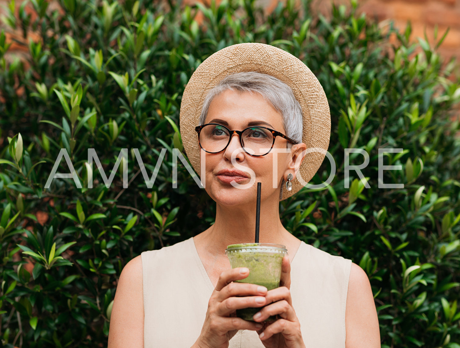 Stylish mature woman in a straw hat wearing eyeglasses holding a cocktail