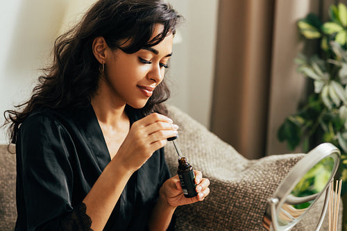 Young woman sitting on a couch holding a bottle with serum preparing for applying