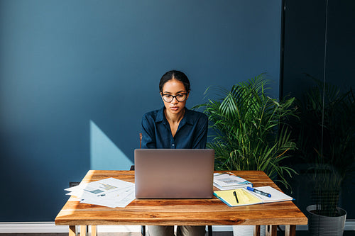 Serious woman sitting at a table and working remotely on a laptop from home