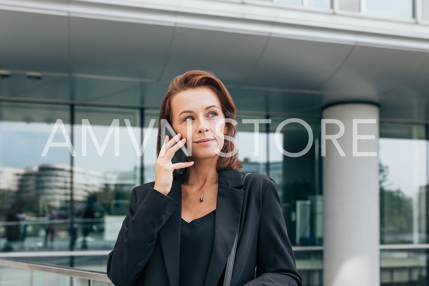 Portrait of a middle-aged female in formal wear talking on a mobile phone against an office building