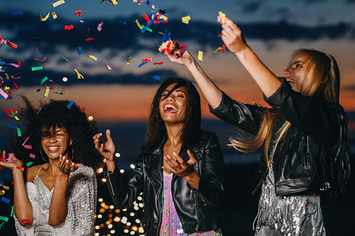 Laughing women throwing confetti at sunset. Three smiling friends having fun together.