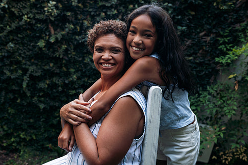 Smiling girl and her grandma looking at the camera. Grandmother and granddaughter hugging outdoors.