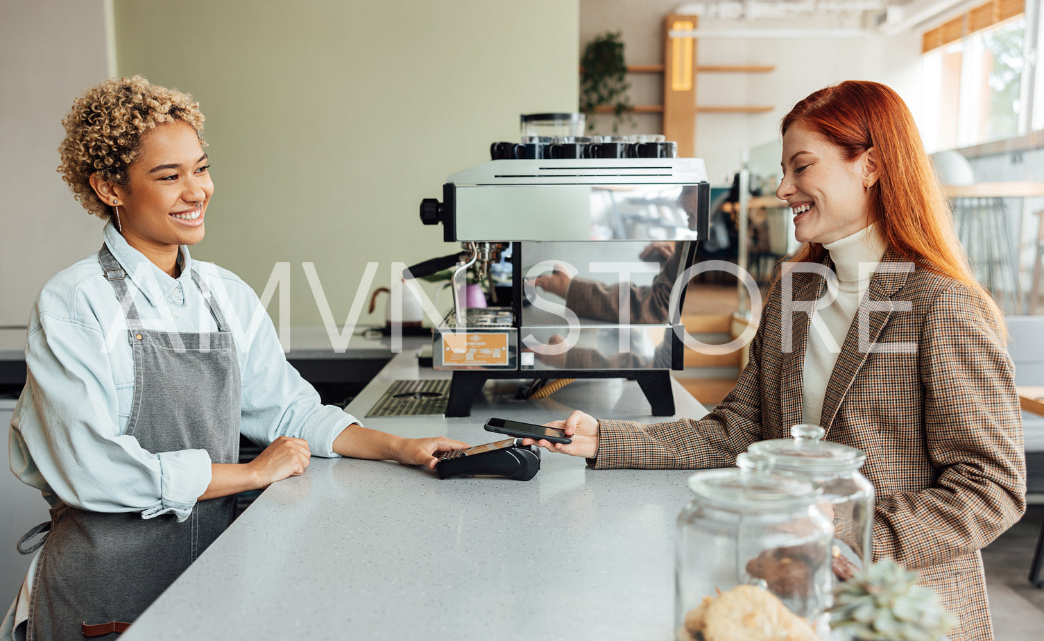 Happy client paying by mobile phone in a coffee shop. Side view of a business owner and a client making a transaction.