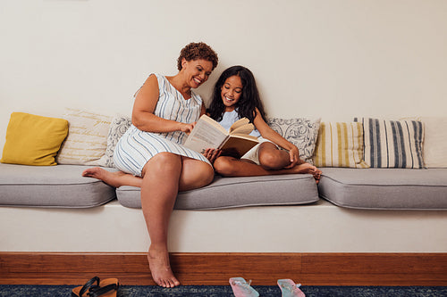 Mature woman reading to her granddaughter. Granny and a kid sitting on a couch.