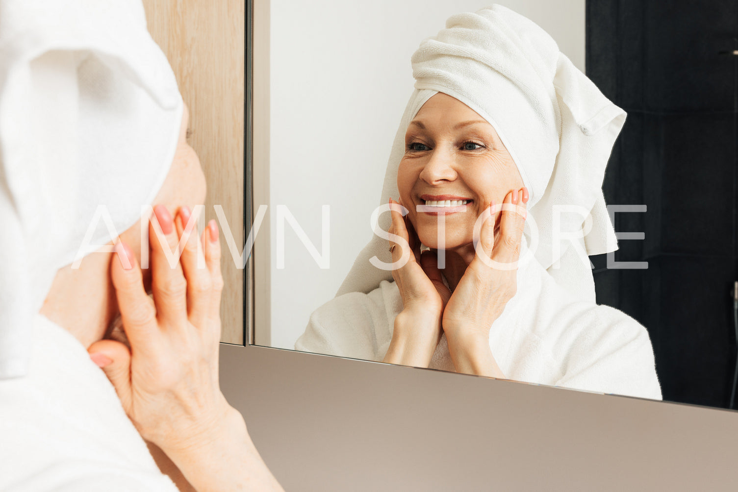 Portrait of a senior female with a towel on her head. Aged woman touching face in front on a mirror.