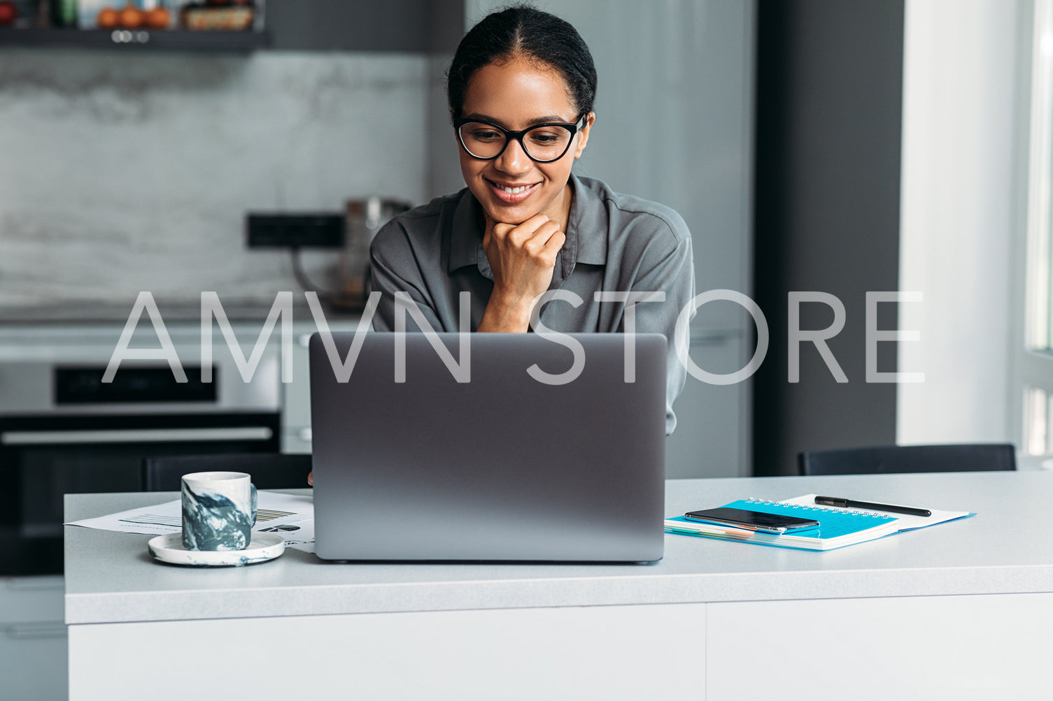 Female entrepreneur working at home office. Smiling woman standing at desk in kitchen and looking on a laptop screen.