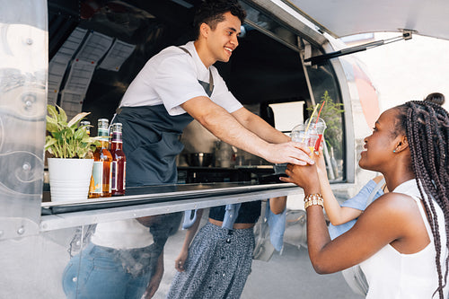 Side view of women buying drinks from a male owner at a food truck