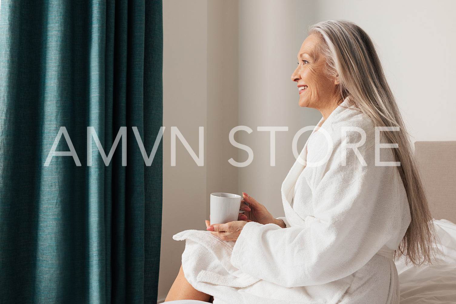 Senior woman sitting on bed in bedroom and looking away. Side view of pensive mature female.