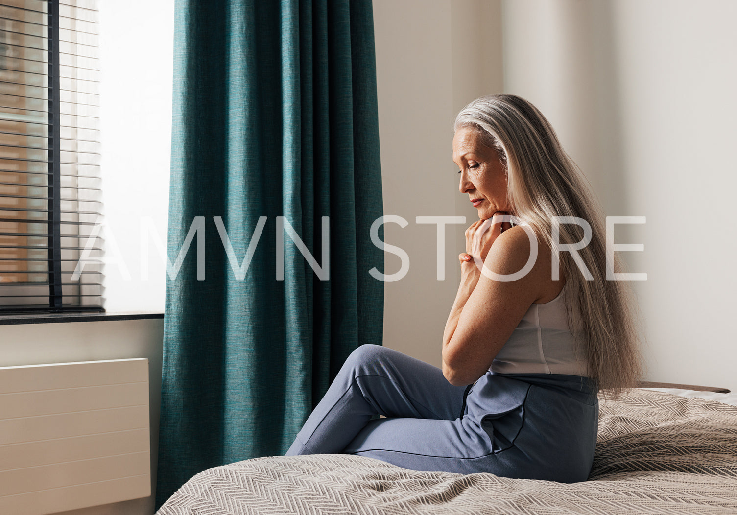 Sad senior woman sitting on a bed. Lonely depressed old female looking down in the bedroom.